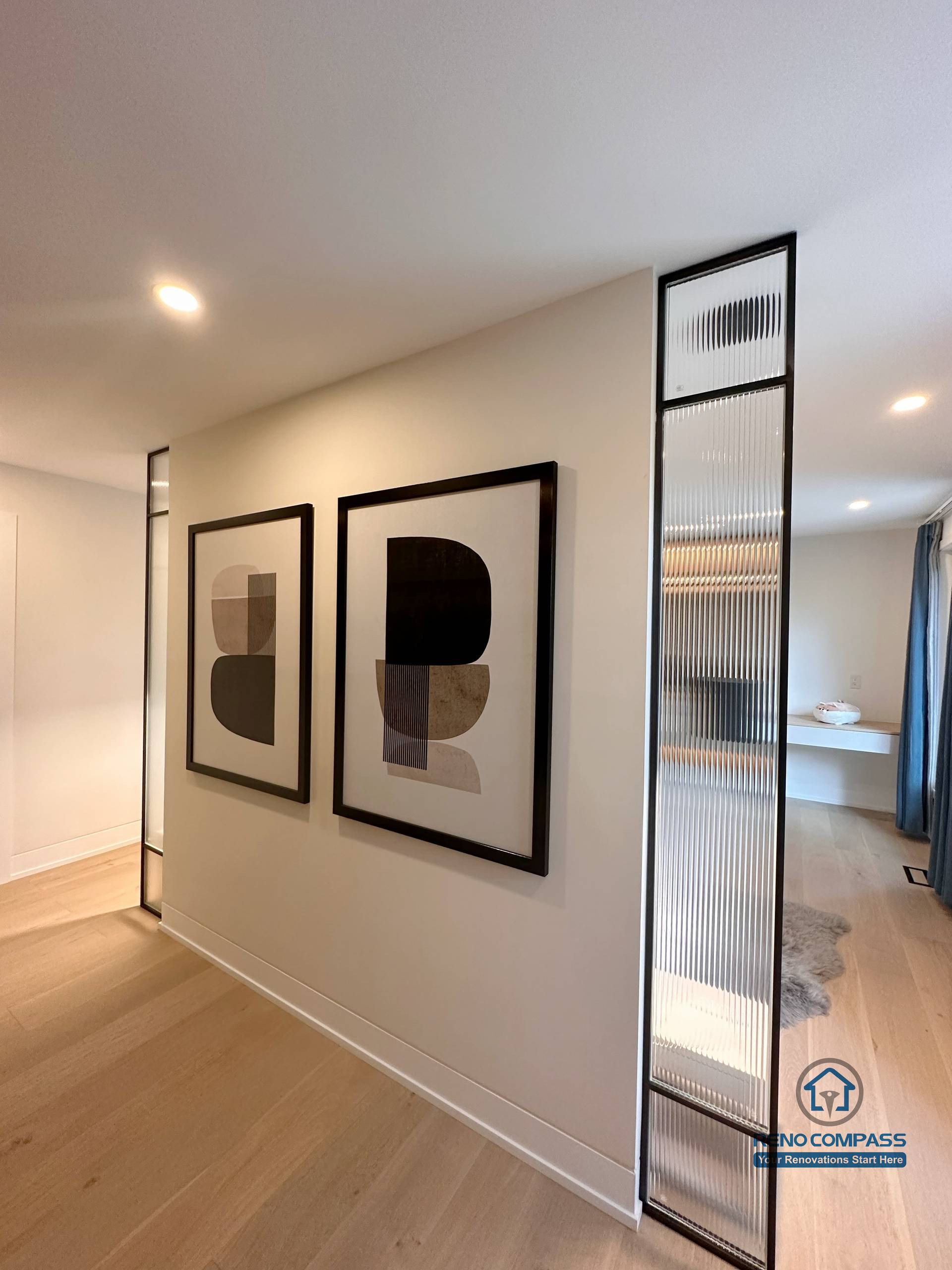 This Toronto interior renovation highlights a modern hallway design with light hardwood flooring, minimalist wall art, and slim glass panel accents that add visual depth while preserving openness. The clean lines and seamless flooring installation enhance continuity between spaces, reflecting refined craftsmanship ideal for contemporary Toronto home renovations.