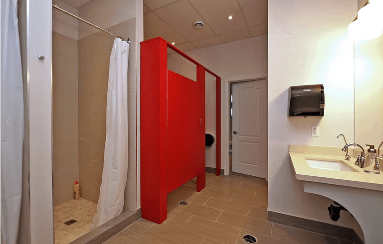 This Richmond Hill yoga studio renovation features a modern change room and shower area designed for comfort, privacy, and durability. The space includes tiled walk-in showers with clean finishes, bold red privacy partitions, non-slip flooring, and a functional vanity area with wall-mounted sink and dispenser. The layout maximizes hygiene, safety, and user convenience while maintaining a sleek commercial aesthetic. As a trusted Toronto renovation company, Reno Compass specializes in high-quality commercial renovations for yoga studios, fitness centers, and wellness facilities, delivering practical and visually appealing interior upgrades.