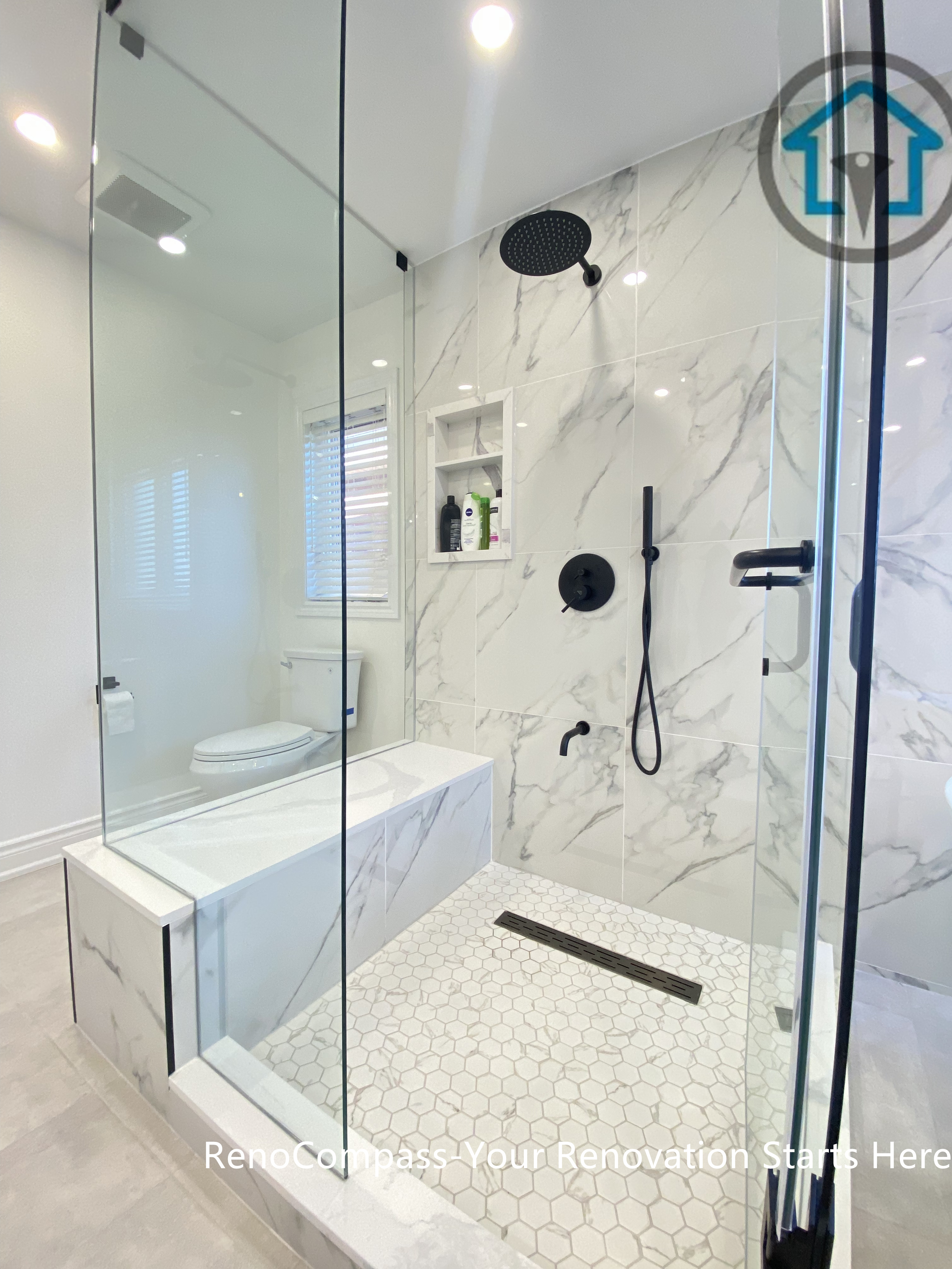 Contemporary Oakville bathroom renovation showcasing a frameless glass walk-in shower, marble-look wall tiles, matte black rain shower system, and hexagon mosaic shower floor. This bathroom remodel highlights precise detailing, clean drainage design, and a modern spa-style layout completed by an experienced Toronto renovation company.
