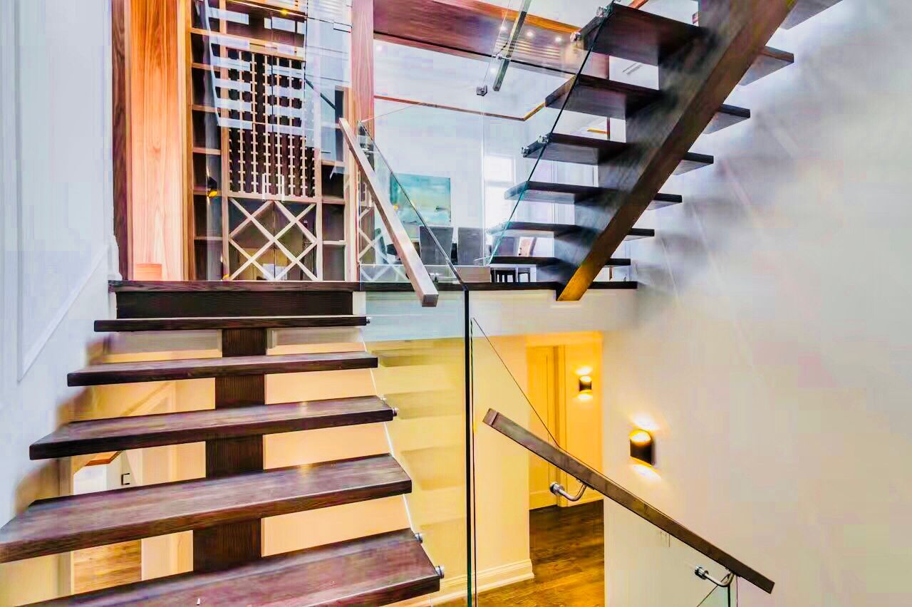 This interior view showcases the precision of modern residential architecture. Featuring a wood-and-glass open-riser staircase and a designer wine storage feature, this project demonstrates how to maximize light and visual flow in a luxury Toronto custom home.