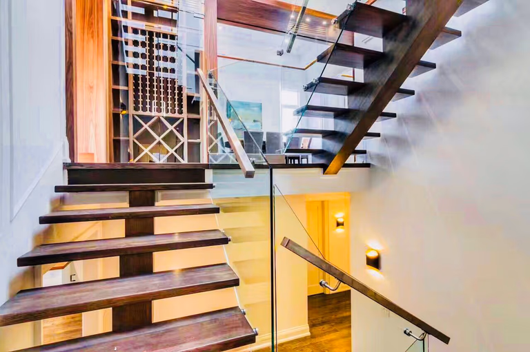 This interior view showcases the precision of modern residential architecture. Featuring a wood-and-glass open-riser staircase and a designer wine storage feature, this project demonstrates how to maximize light and visual flow in a luxury Toronto custom home.