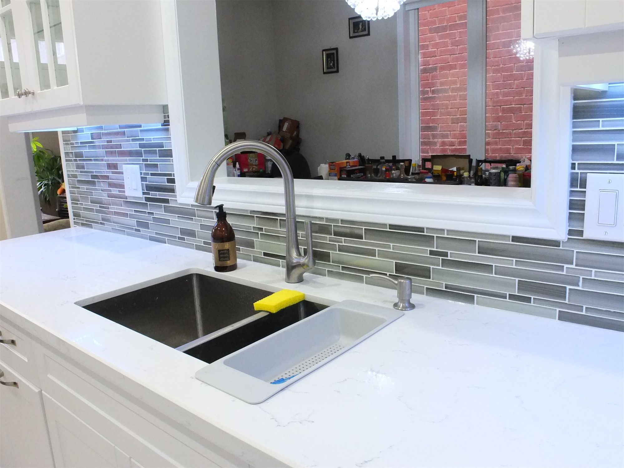 This Vaughan kitchen renovation features elegant white shaker cabinets with glass display doors, quartz countertops, and a stylish mosaic tile backsplash with LED under-cabinet lighting. The pass-through opening above the sink connects the kitchen to the dining area, creating a brighter and more open layout. Completed by a professional Toronto renovation company, the design blends modern functionality with clean, timeless aesthetics.