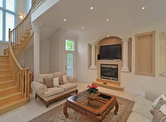 Elegant luxury living room interior from a custom Toronto home renovation featuring a classic fireplace design, decorative columns, curved staircase, and spacious seating area. The bright open-concept layout highlights refined architectural details, natural lighting, and timeless interior finishes. This interior renovation project was completed by Reno Compass, a trusted Toronto Renovation Company specializing in luxury home rebuilds and custom interior renovations across the Greater Toronto Area.