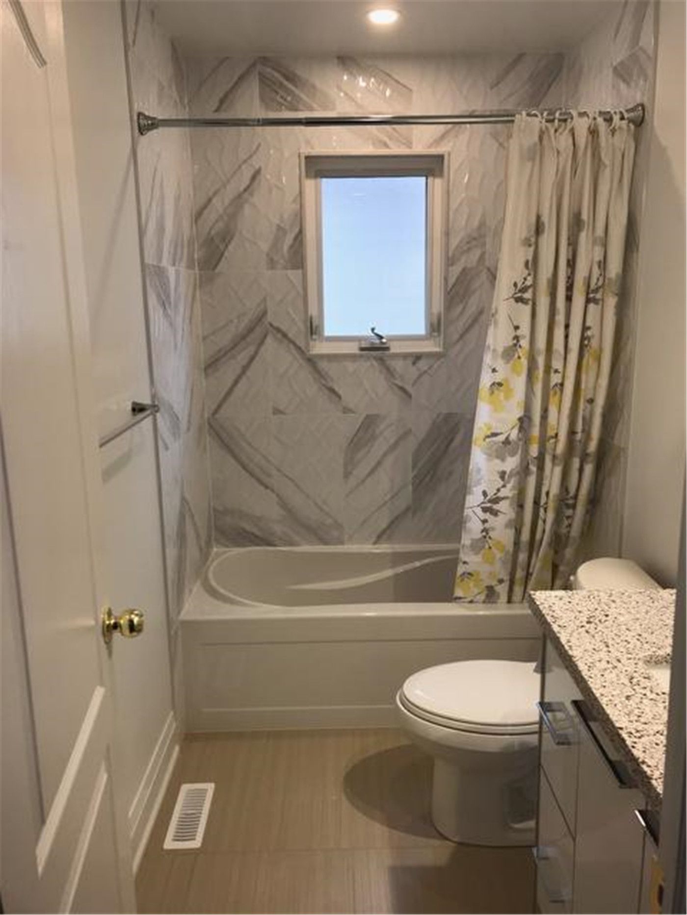This North York bathroom renovation features a compact yet fully functional layout with a bathtub, chevron-pattern tile wall, and a window that brings in natural light. The design combines durable finishes, efficient space planning, and clean lines to create a comfortable and easy-to-maintain family bathroom.