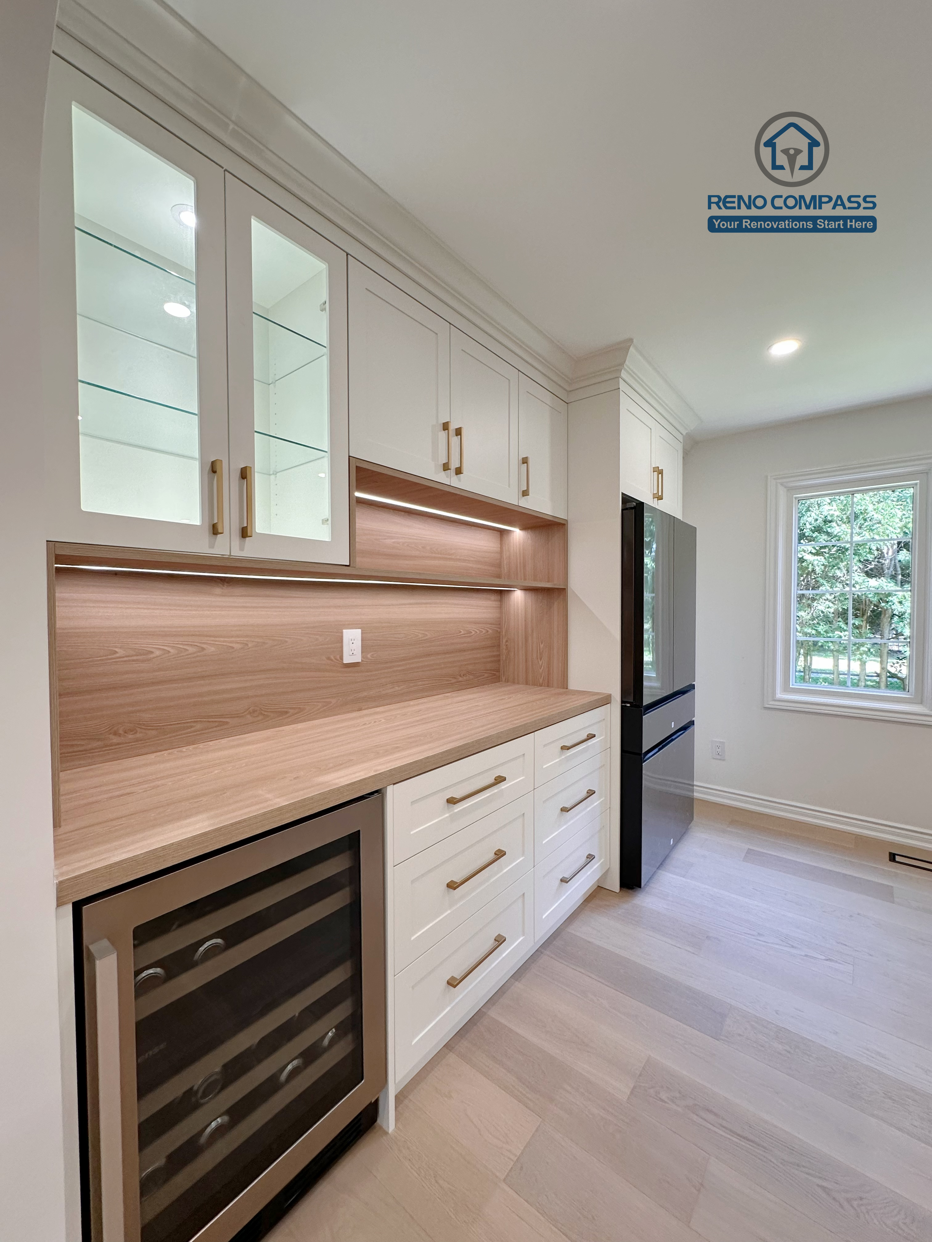 This Markham kitchen renovation features custom white cabinetry with integrated glass display cabinets, warm wood backsplash panels, and built-in storage solutions. Under-cabinet lighting enhances functionality while highlighting material textures and clean detailing. Completed by a professional Toronto renovation company, Reno Compass Inc., the design balances storage efficiency with refined craftsmanship.