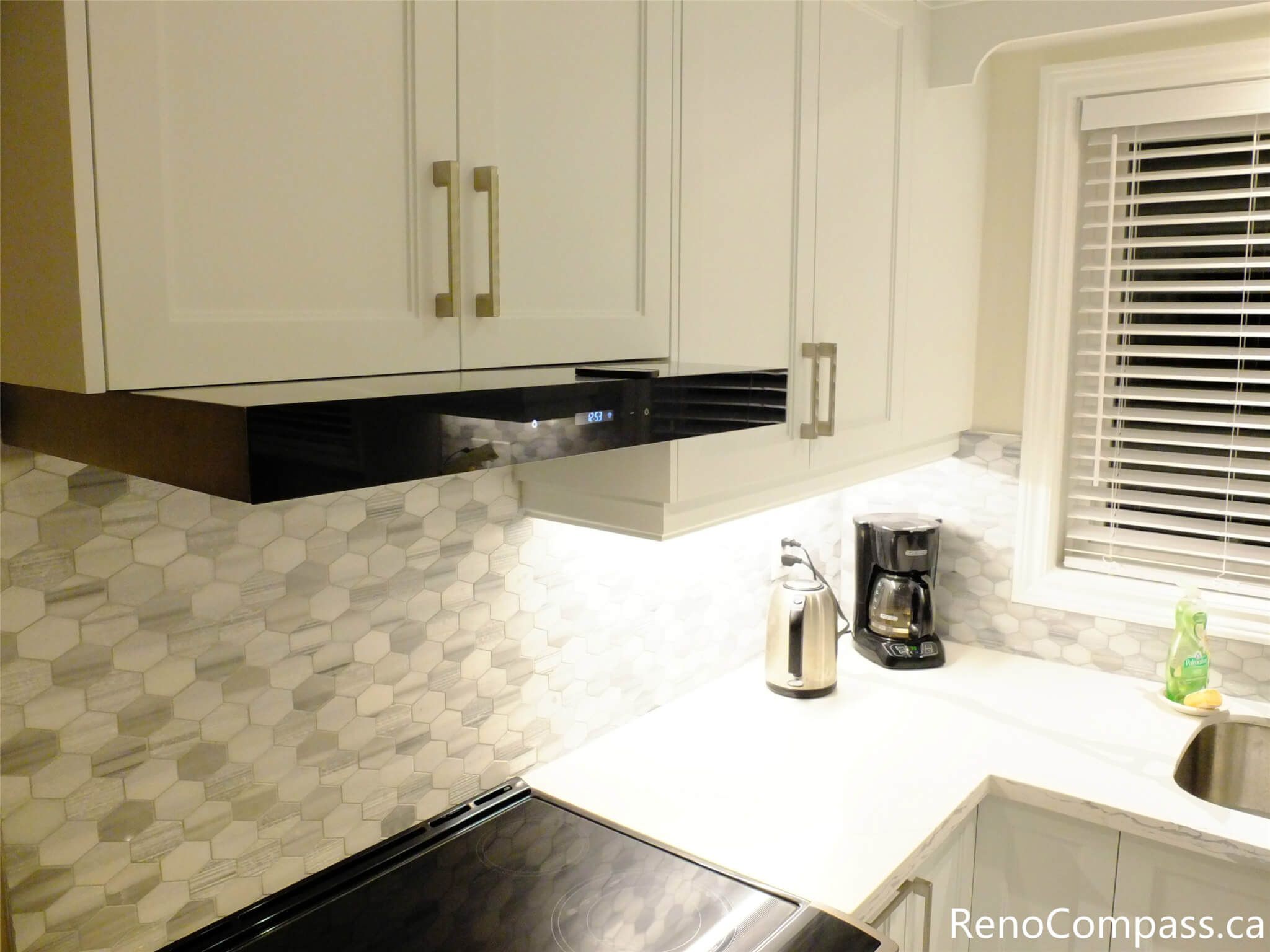This North York kitchen renovation showcases custom white cabinetry, a sleek built-in range hood, and a hexagon tile backsplash that adds texture and visual depth. The clean countertop lines and efficient cooking layout enhance everyday functionality, completed by a professional Toronto renovation company.