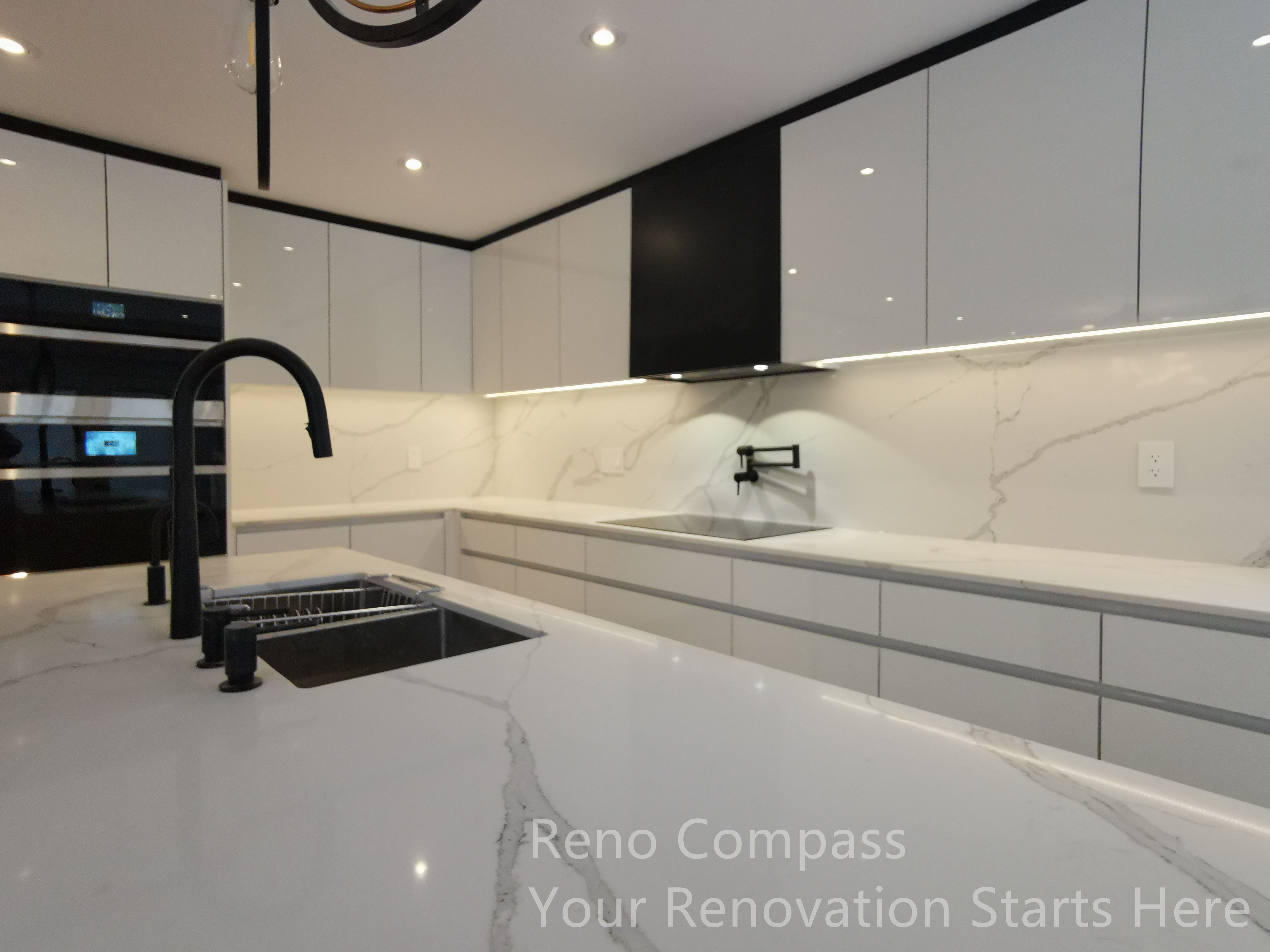 This image captures the completed kitchen island and main work area in a Markham interior renovation. The oversized stone island provides generous workspace and seating potential, while the integrated sink and matte black faucet add a bold, modern contrast. Handle-less custom cabinetry, full-height stone backsplash, and under-cabinet lighting create a seamless and refined look, combining visual clarity with everyday functionality in this contemporary kitchen design.