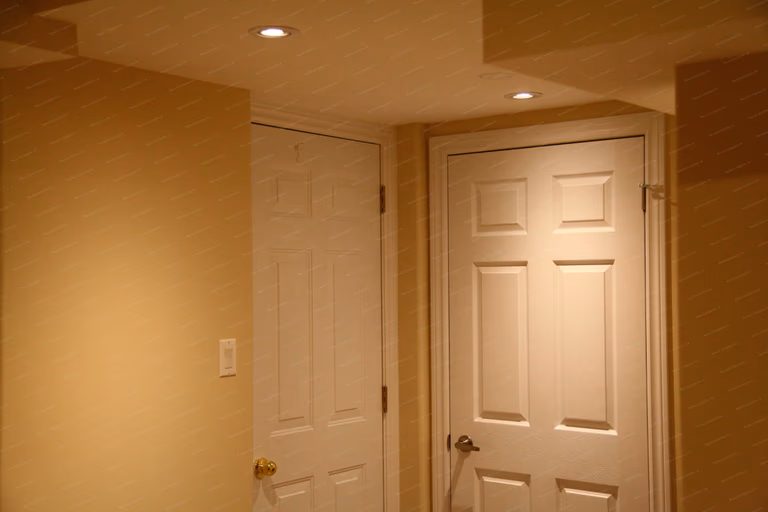 This image features the interior doors and hallway area in a finished basement renovation in Markham. Cleanly installed panel doors, smooth wall finishes, and recessed ceiling lighting create a well-defined circulation space while maintaining a cohesive look throughout the basement. Attention to door alignment and finishing details ensures both functionality and visual consistency, completed by a professional Toronto renovation company.