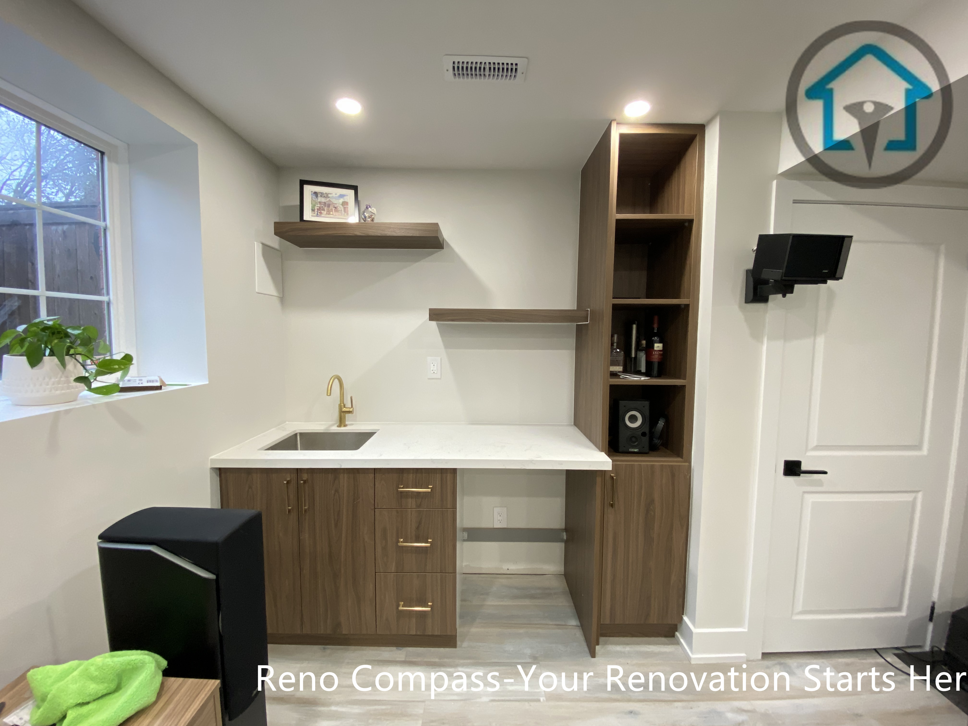 This Stouffville basement renovation features a modern kitchenette with custom wood cabinetry, quartz countertop, integrated sink, open shelving, and built-in storage. Designed and built by Reno Compass Inc., this basement upgrade enhances functionality and adds long-term value with clean lines and efficient space planning.