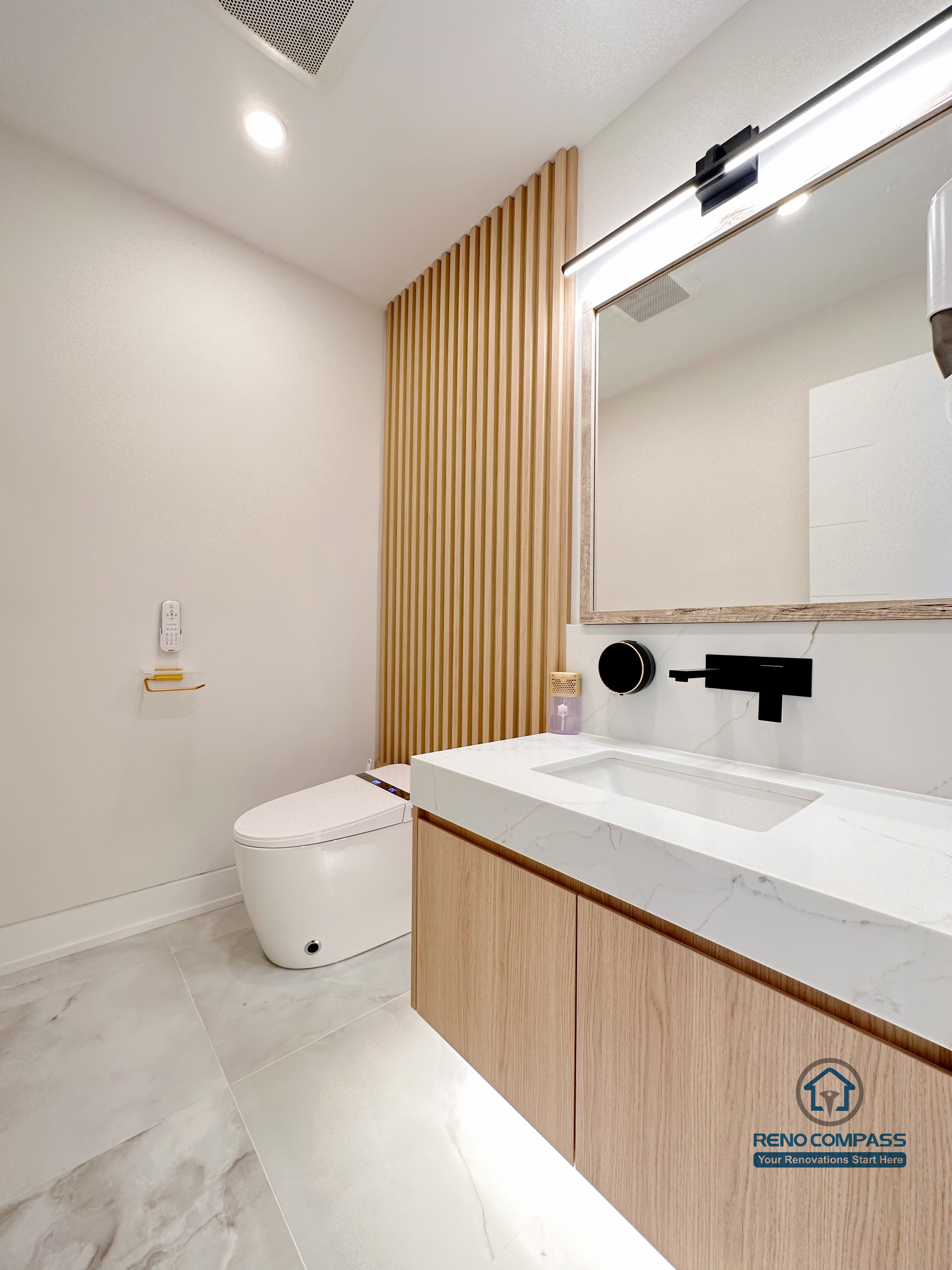 Contemporary bathroom renovation in Toronto featuring a custom wood-grain vanity, integrated sink, modern wall-mounted faucet, vertical wood slat accent wall, and soft neutral finishes. Completed by a professional Toronto renovation company with a focus on warm minimalism and refined detailing.