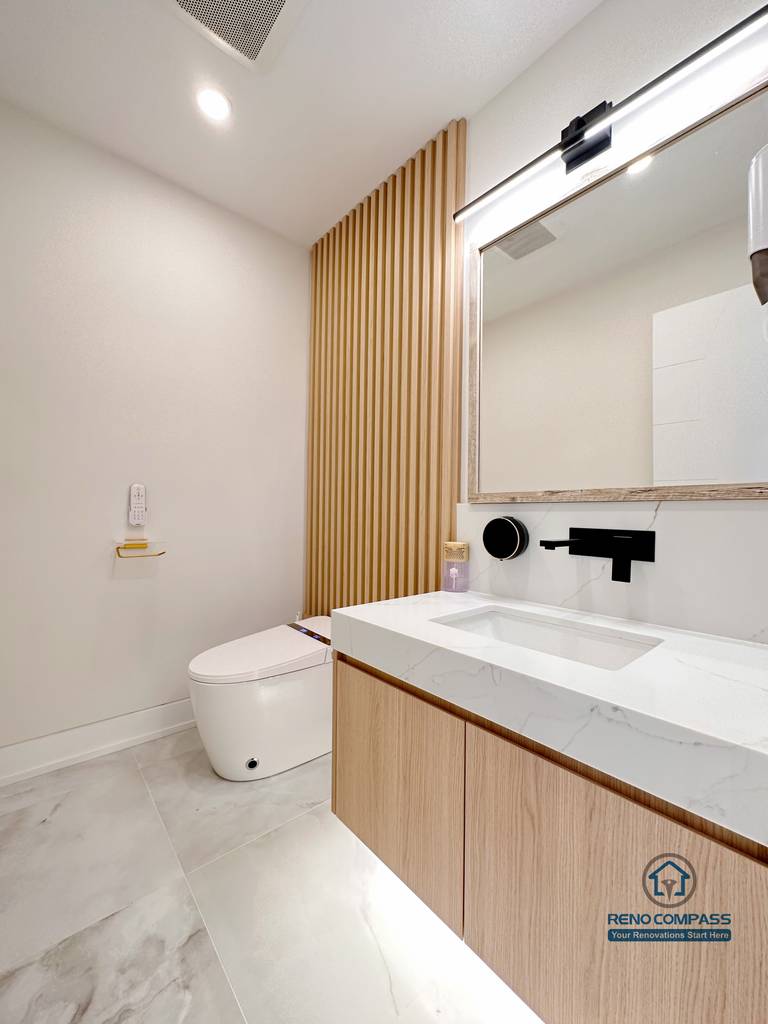 Contemporary bathroom renovation in Toronto featuring a custom wood-grain vanity, integrated sink, modern wall-mounted faucet, vertical wood slat accent wall, and soft neutral finishes. Completed by a professional Toronto renovation company with a focus on warm minimalism and refined detailing.