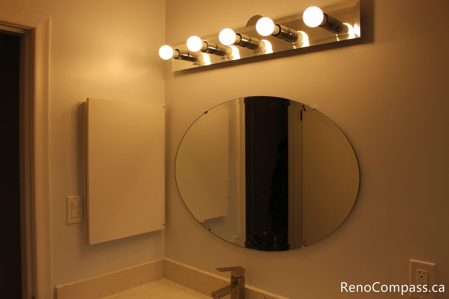 Modern bathroom lighting upgrade featuring a classic bulb vanity light bar and oval pivot mirror. Part of a full bathroom refresh in Oshawa by RenoCompass.ca, focusing on bright, functional, and stylish grooming spaces.