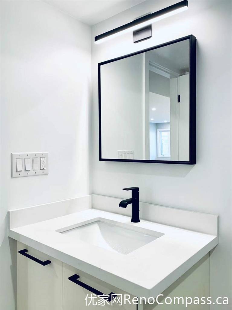 This bathroom from a Markham full home renovation showcases a sleek vanity design with an integrated sink, matte black faucet, and a clean-lined mirror with LED lighting. The minimalist white cabinetry paired with black accents creates a sharp, modern contrast while maintaining a bright and functional space.