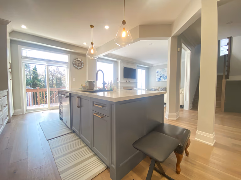 An open-concept kitchen island designed as part of a Richmond Hill interior renovation, featuring integrated seating, custom cabinetry, quartz countertops, and warm pendant lighting. The island functions as a central hub for cooking, casual dining, and family interaction, seamlessly connecting the kitchen to adjacent living spaces.