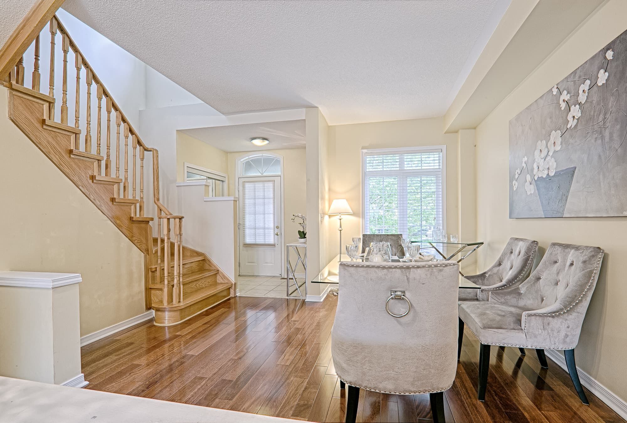 This open living room showcases a simple and lovely interior design with warm hardwood flooring, a classic fireplace, and a balanced open-concept layout. The neutral color palette, soft area rug, and coordinated furniture styling create a comfortable and inviting atmosphere. The seamless connection between the living and dining areas enhances openness and flow, making this space ideal for modern family living and entertaining.