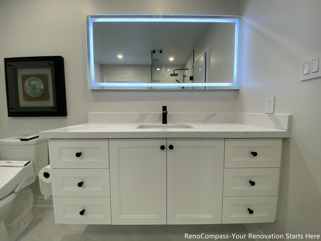 This Markham bathroom renovation features a full-width vanity with classic white cabinetry, a seamless white countertop, and an integrated LED mirror. The symmetrical layout improves daily usability and storage efficiency, while soft lighting and neutral finishes keep the space bright and uncluttered. Matte black hardware adds subtle contrast, creating a clean and timeless bathroom design.
City: Markham · Toronto contractor: Reno Compass