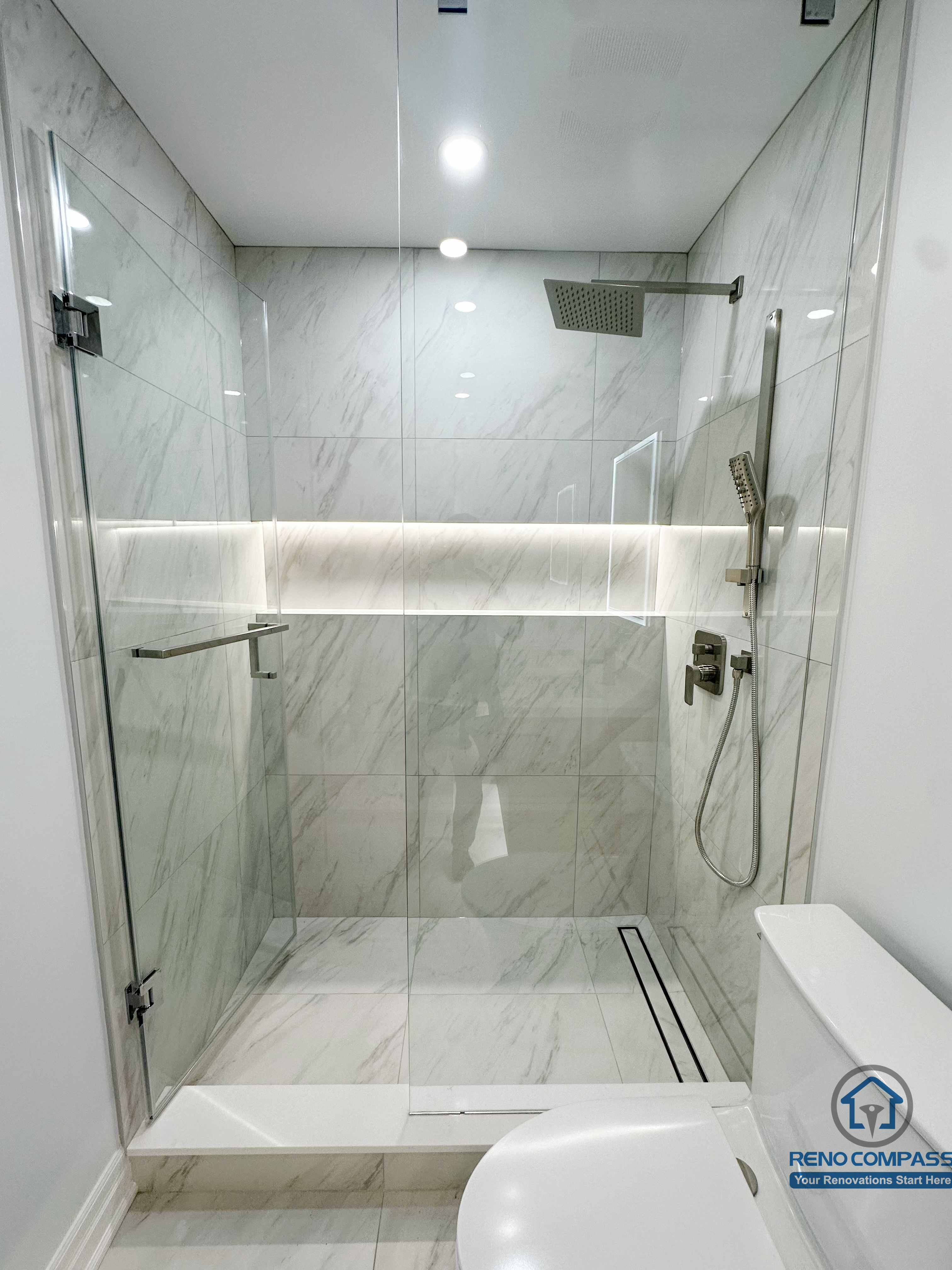 Minimalist walk-in shower featuring frameless glass panels, marble-look porcelain tiles, a linear floor drain, and an integrated LED-lit niche that adds both functionality and a subtle sense of luxury.