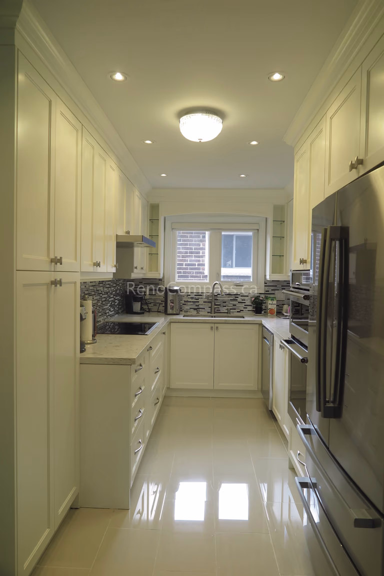 This Toronto interior renovation features a bright modern kitchen with custom white cabinetry, quartz countertops, built-in stainless steel appliances, and a stylish mosaic backsplash. The efficient layout maximizes storage and functionality while maintaining a clean, elegant look. Completed by a trusted Toronto renovation contractor, this project reflects Reno Compass Inc.’s expertise in delivering high-quality kitchen upgrades and refined interior finishes.