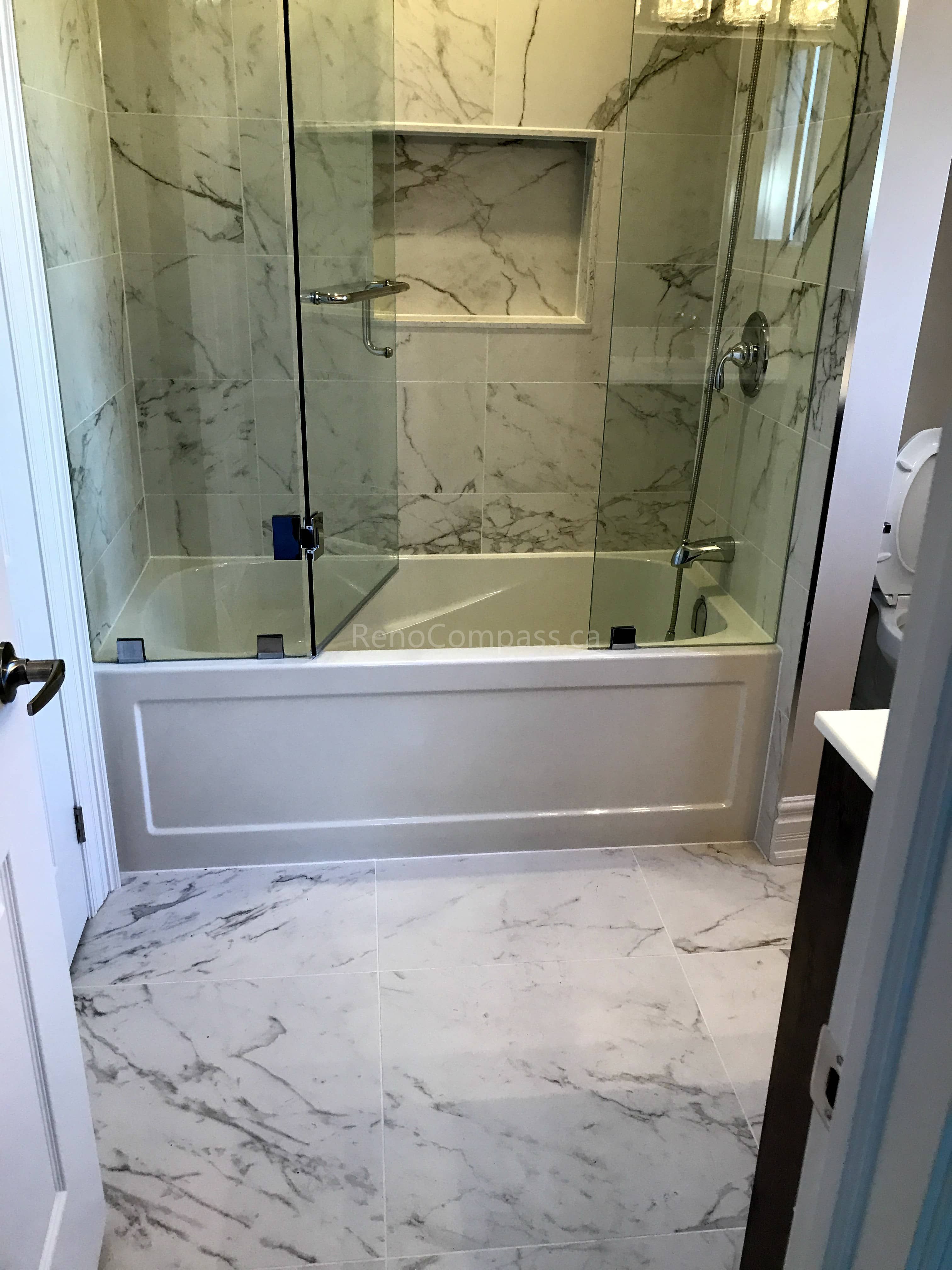 This Toronto bathroom renovation by Reno Compass showcases a modern marble-inspired design with full-height wall tiles and matching marble-look floor tiles for a seamless, elegant finish. The bathtub is upgraded with a frameless glass enclosure, enhancing both safety and visual openness. A built-in wall niche provides practical storage while maintaining a clean look. High-quality fixtures and precise tile installation create a bright, durable, and sophisticated bathroom space designed for long-term comfort and style.