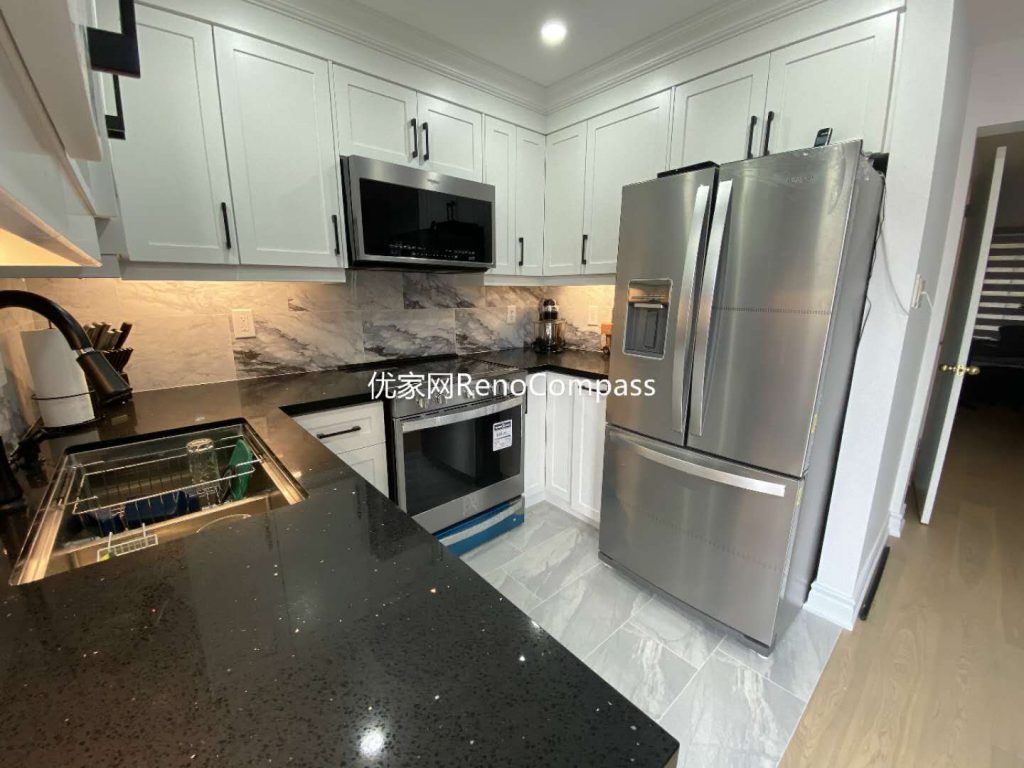 This image features a completed kitchen renovation project in Mississauga, highlighting full-height white shaker cabinets, quartz countertops, and a modern stainless steel appliance package. The functional L-shaped layout maximizes workspace efficiency, while the integrated microwave, built-in oven, and French-door refrigerator create a clean and cohesive appearance. Subtle under-cabinet lighting and stone-pattern backsplash add depth and warmth to the space, balancing practicality with modern aesthetics. The renovation emphasizes durability, efficient storage, and everyday usability, demonstrating the quality craftsmanship of a professional Toronto renovation company.