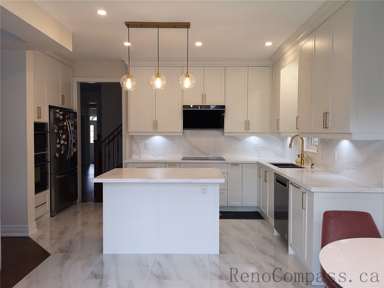 This Aurora kitchen renovation showcases a bright open-concept design featuring custom white shaker cabinets, quartz countertops, and a functional center island. Elegant pendant lighting, marble-style flooring, and brushed gold fixtures add warmth and sophistication to the modern space. Completed by a professional Toronto renovation company focused on quality craftsmanship, efficient layout planning, and timeless interior design.
