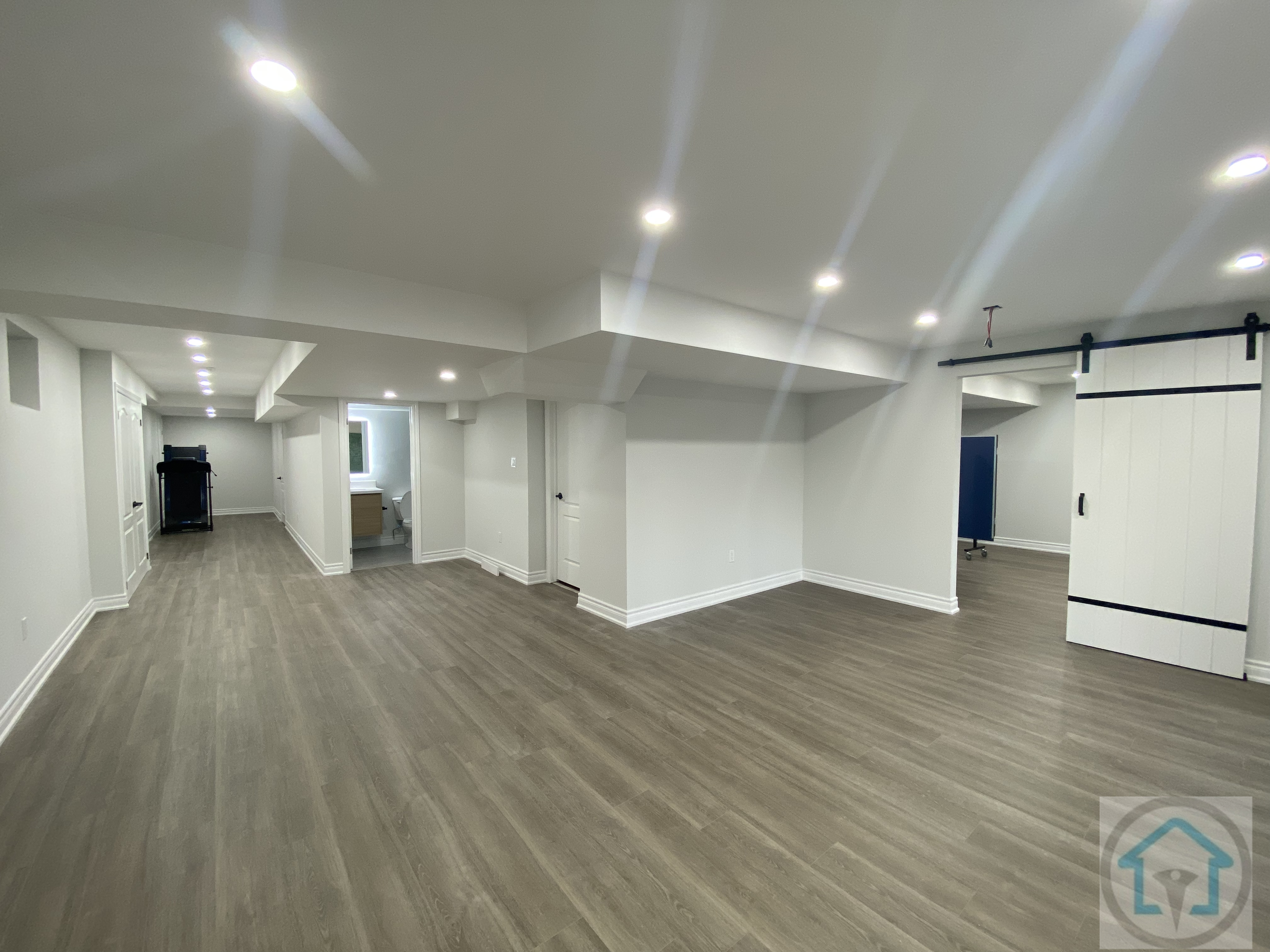 This Aurora basement renovation features an open-concept layout with modern flooring, bright recessed lighting, and clean white walls. The design maximizes natural light and creates a versatile living space suitable for family activities or entertainment. Contractor: Reno Compass Inc., City: Aurora.