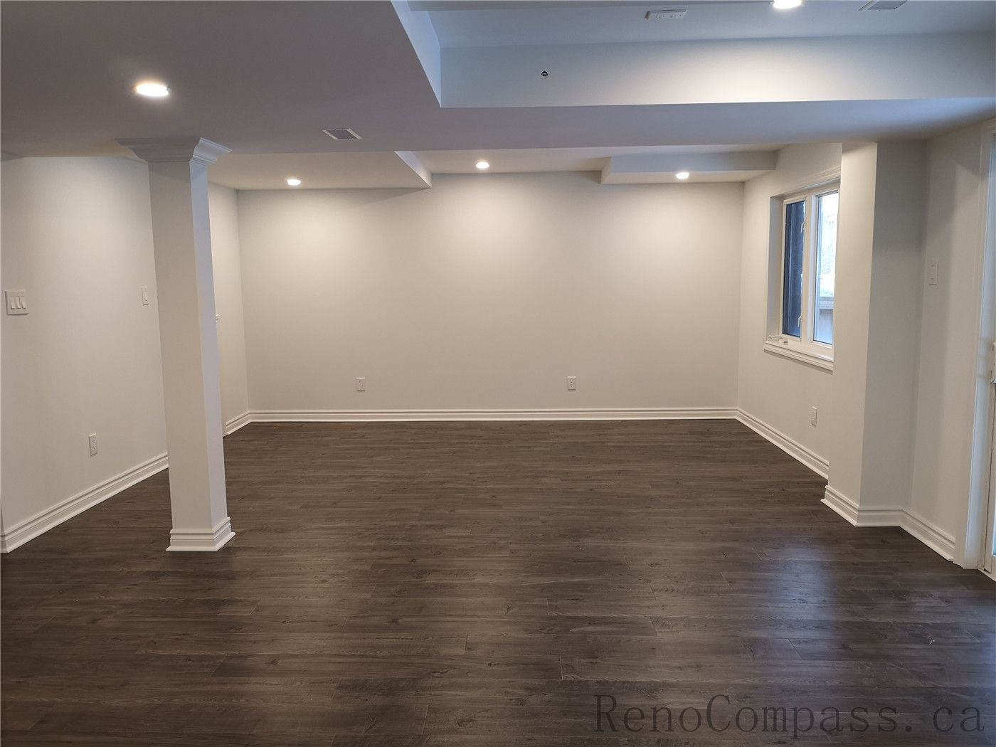 This Richmond Hill basement renovation showcases a spacious open-concept layout with newly installed dark wood flooring, pot lights, and clean modern finishes. Structural columns were integrated seamlessly into the design to maintain an open and functional living space. The upgraded lighting and neutral wall tones create a warm and inviting basement environment ideal for family use or entertainment. Completed by a professional Toronto renovation company, Reno Compass Inc., this finished basement delivers both comfort and contemporary style.
