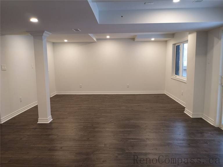 This Richmond Hill basement renovation showcases a spacious open-concept layout with newly installed dark wood flooring, pot lights, and clean modern finishes. Structural columns were integrated seamlessly into the design to maintain an open and functional living space. The upgraded lighting and neutral wall tones create a warm and inviting basement environment ideal for family use or entertainment. Completed by a professional Toronto renovation company, Reno Compass Inc., this finished basement delivers both comfort and contemporary style.