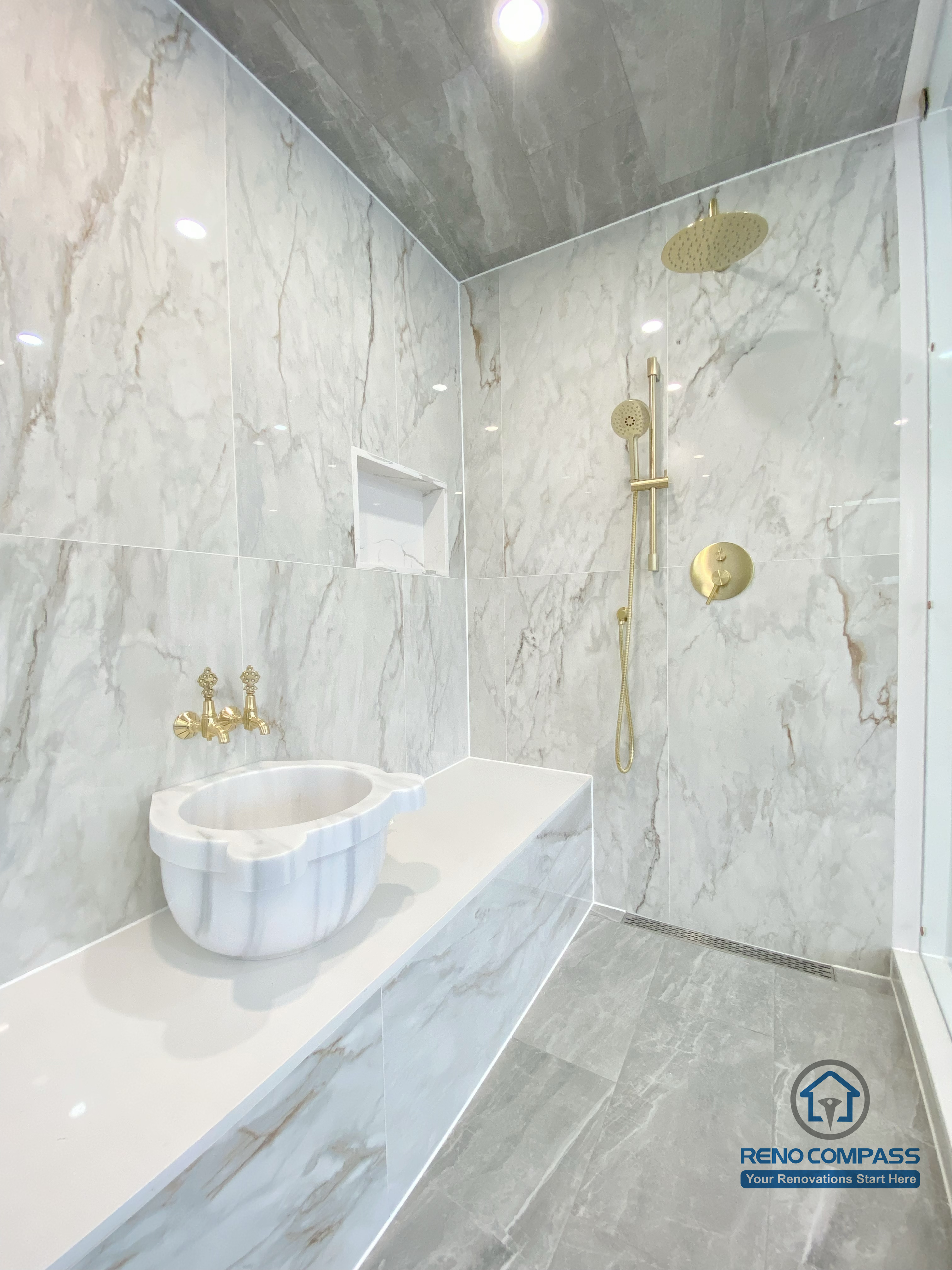This Richmond Hill bathroom renovation features a modern walk-in shower finished with full-height marble-style wall tiles, a custom built-in bench, and a recessed wall niche for added functionality. Gold-finish shower fixtures and rain shower head create a refined, spa-inspired look, while large-format floor tiles enhance durability and visual continuity. This image highlights detailed craftsmanship and high-end material selection in a luxury bathroom renovation project in Richmond Hill.