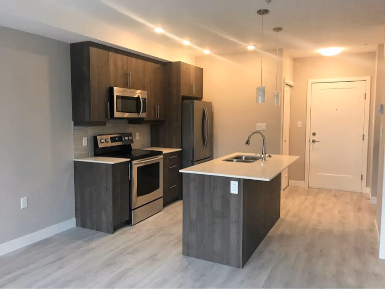 This Oakville condo kitchen renovation showcases a modern open-concept layout featuring a sleek center island, quartz countertop, and contemporary wood-tone cabinetry. Upgraded stainless steel appliances, pendant lighting, and recessed pot lights enhance both functionality and style. The bright flooring and clean design create a spacious, practical kitchen ideal for modern condo living.