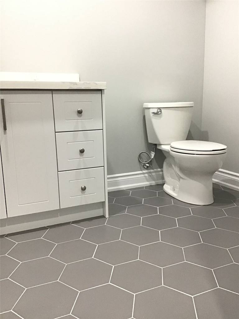 Contemporary basement bathroom renovation in Newmarket featuring grey hexagon floor tiles, white vanity cabinetry, and clean neutral wall finishes. This thoughtfully designed space combines durability, simplicity, and modern style to complete the fully finished basement.