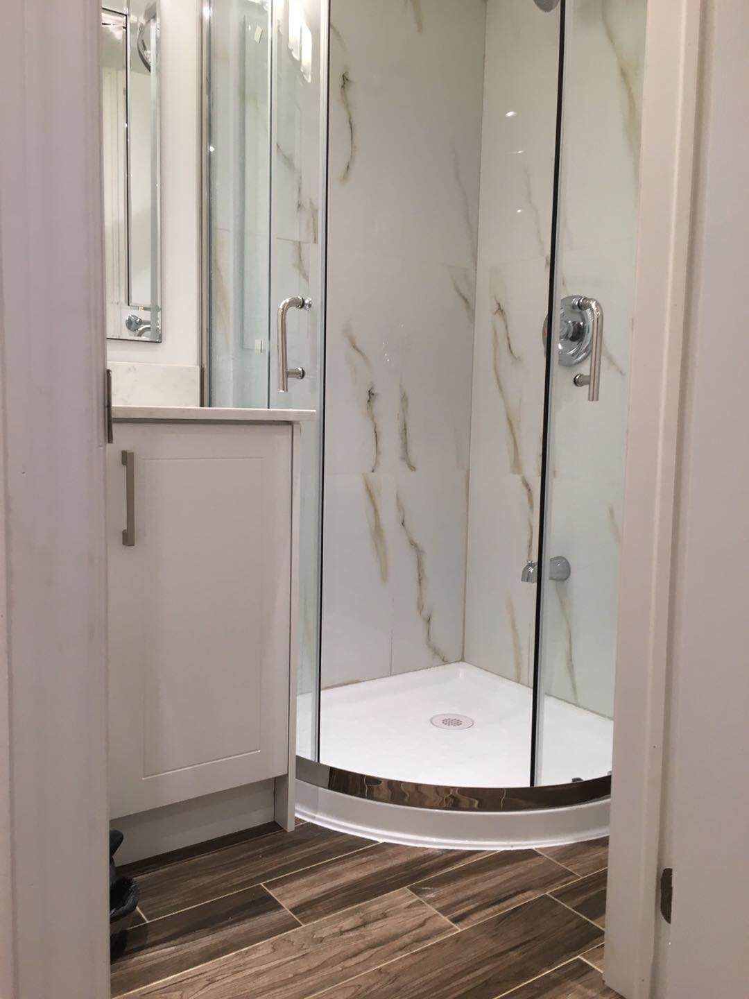 This Markham basement renovation highlights a professionally installed curved glass shower enclosure with marble-look wall panels and modern chrome fixtures. The space-efficient corner shower design enhances functionality while maintaining a clean, contemporary aesthetic ideal for basement bathrooms in Markham homes.