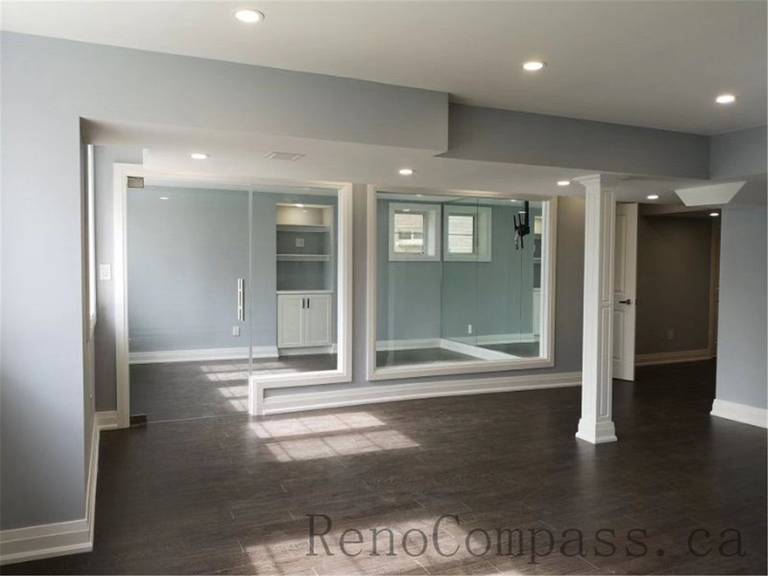 An open-concept basement in Aurora redesigned with soft gray tones, recessed lighting, and sleek trim work. The minimalist, modern aesthetic creates a bright and inviting lower-level living space — completed by Reno Compass.
