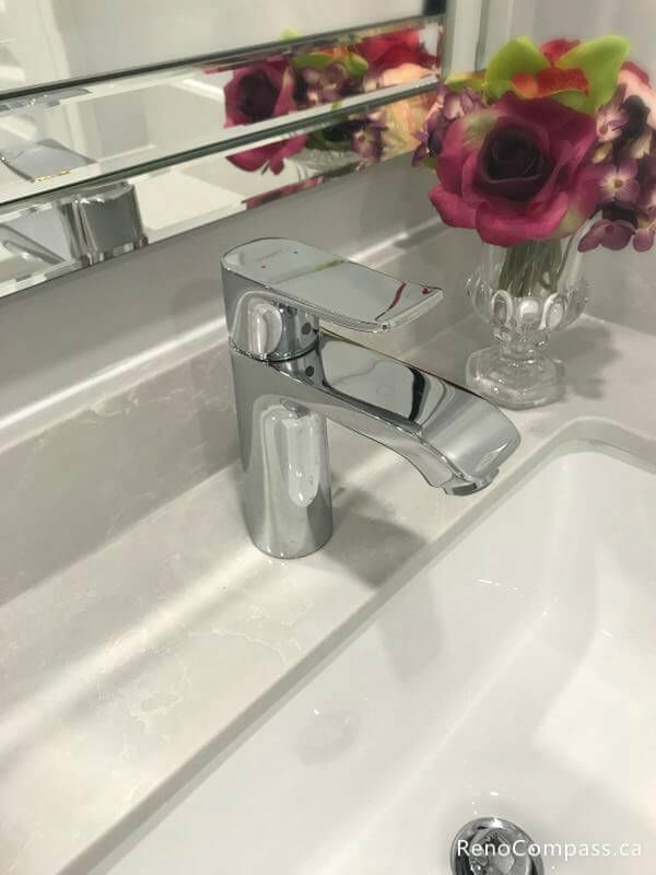 A close-up of a sleek, modern chrome single-handle faucet installed on a white marble-patterned quartz countertop. High-quality finishes from a professional Markham bathroom renovation.