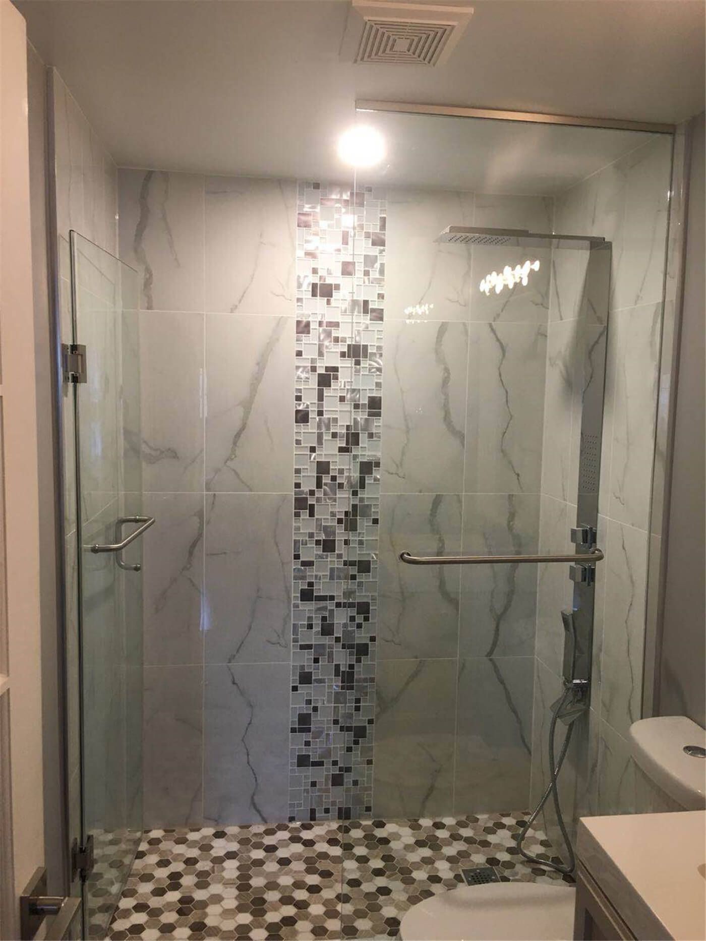 This walk-in shower renovation in Newmarket features elegant marble-pattern wall tiles paired with smaller accent mosaic tiles that divide the shower space visually. The combination of large marble surfaces and detailed tile accents creates a modern, layered look while maintaining a bright and clean bathroom design.