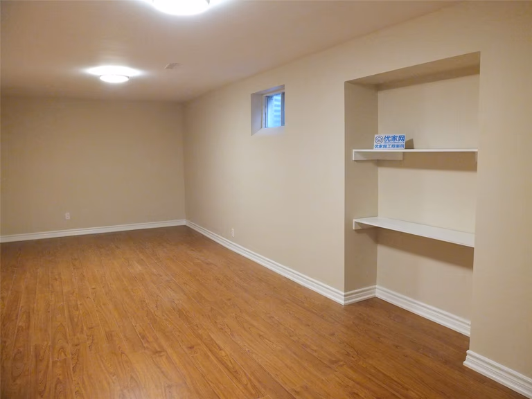 This Markham basement renovation includes a custom built-in wall shelving unit designed to add practical storage and display space. The recessed niche with clean white shelves contrasts beautifully with the warm neutral wall paint and wood-style flooring, creating a functional and visually balanced interior feature. The installation enhances basement organization while maintaining a modern and tidy interior design.