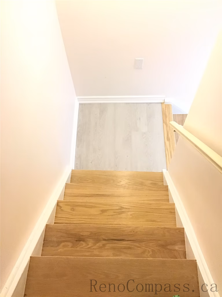 Newly installed modern wooden staircase for this Pickering basement renovation project, featuring natural-tone wood steps, clean white side walls, and a bright contemporary finish. The upgraded basement stairs improve both safety and visual flow, creating a seamless transition to the newly finished lower level. Completed by Reno Compass Inc., a professional Toronto Renovation Company.
