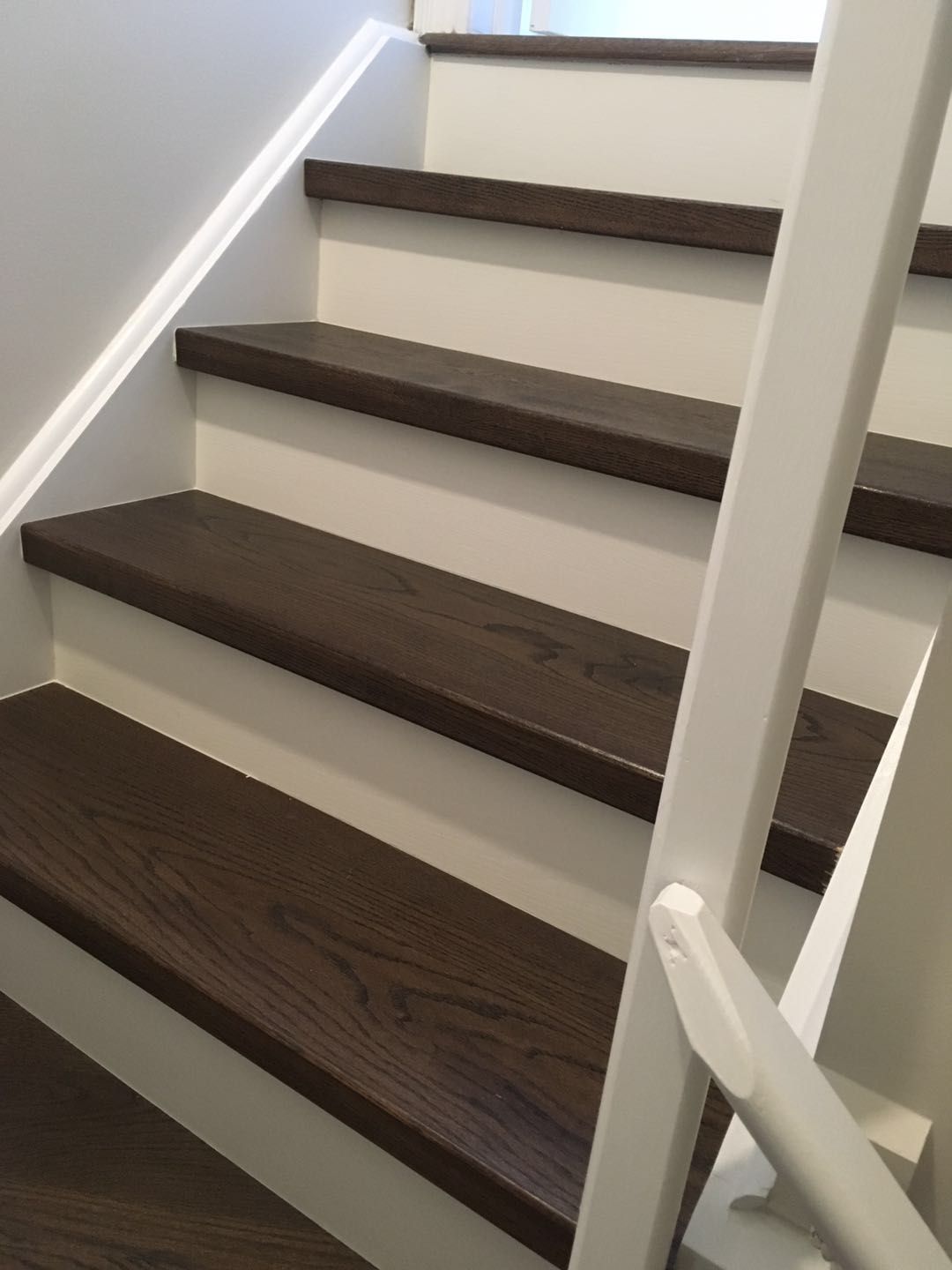This Toronto interior renovation showcases a custom curved staircase featuring rich dark wood treads paired with clean white risers and railings. The design maximizes space efficiency while adding architectural interest, seamlessly connecting levels with a modern yet timeless aesthetic. The surrounding neutral tones and hardwood flooring enhance the overall warmth and flow of the home.