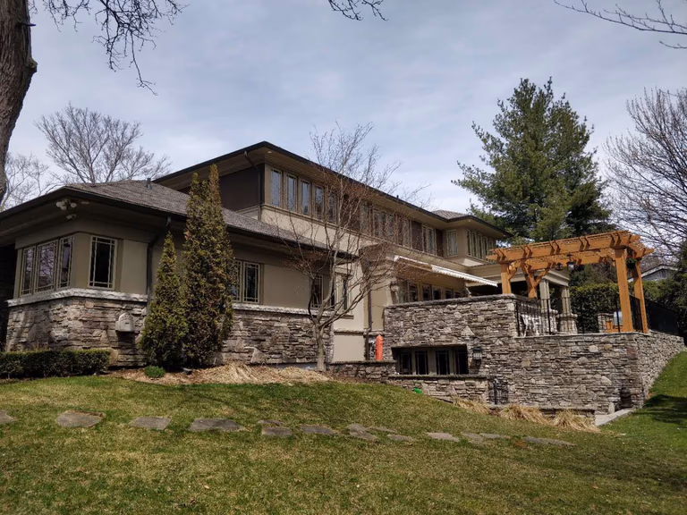 This Oakville landscaping renovation project showcases a beautifully designed backyard featuring natural stone retaining walls, elevated garden structures, and a custom wooden pergola. The layered stonework enhances both structural stability and visual depth, while the pergola creates a defined outdoor living space ideal for relaxation and entertaining.

The sloped lawn was carefully integrated into the landscape design to maintain proper drainage and long-term durability. The combination of natural stone textures and warm wood elements gives the property a refined and timeless exterior appearance.