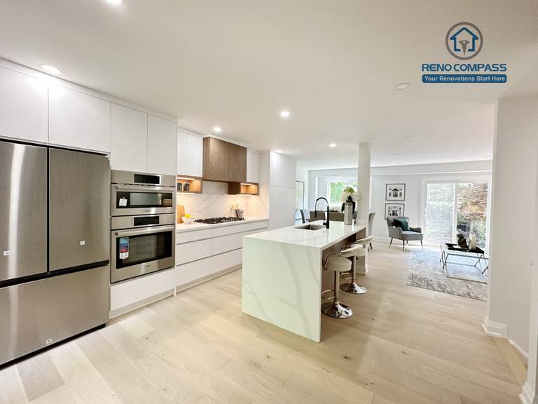 This Richmond Hill interior renovation features a bright open-concept kitchen and living space with custom white cabinetry, integrated stainless steel appliances, a waterfall kitchen island, and wide-plank hardwood flooring. Designed and completed by a Toronto renovation company, the layout enhances natural light, functionality, and modern living comfort for contemporary family homes.