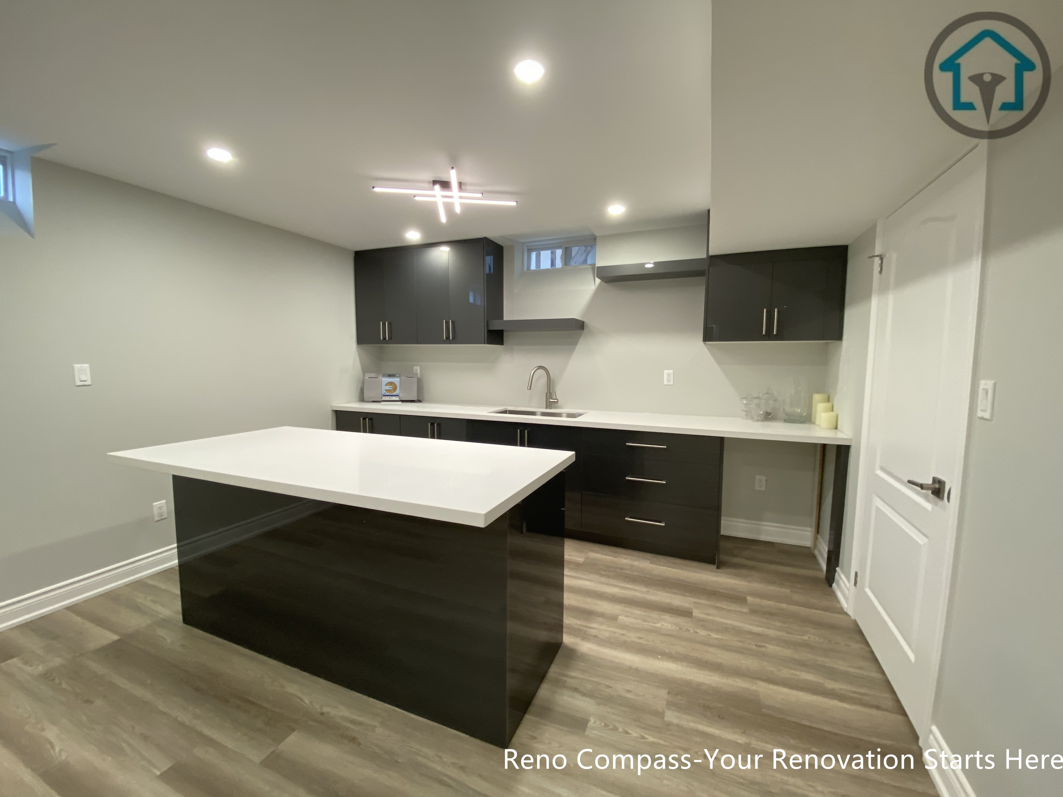 A modern basement kitchen renovation in Markham featuring a large quartz island, custom dark cabinetry, integrated lighting, and durable flooring, creating a functional and stylish lower-level living space.
