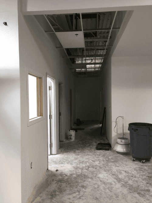 This image shows a hallway construction phase during a commercial retail store renovation, featuring new wall framing, door installation, and suspended ceiling preparation. The space is being prepared for lighting, HVAC, and finishing work to create a clean and functional layout for retail operations. Reno Compass Inc. ensures each stage of the commercial renovation is completed with precision, building a safe, efficient, and modern interior environment for the finished store.