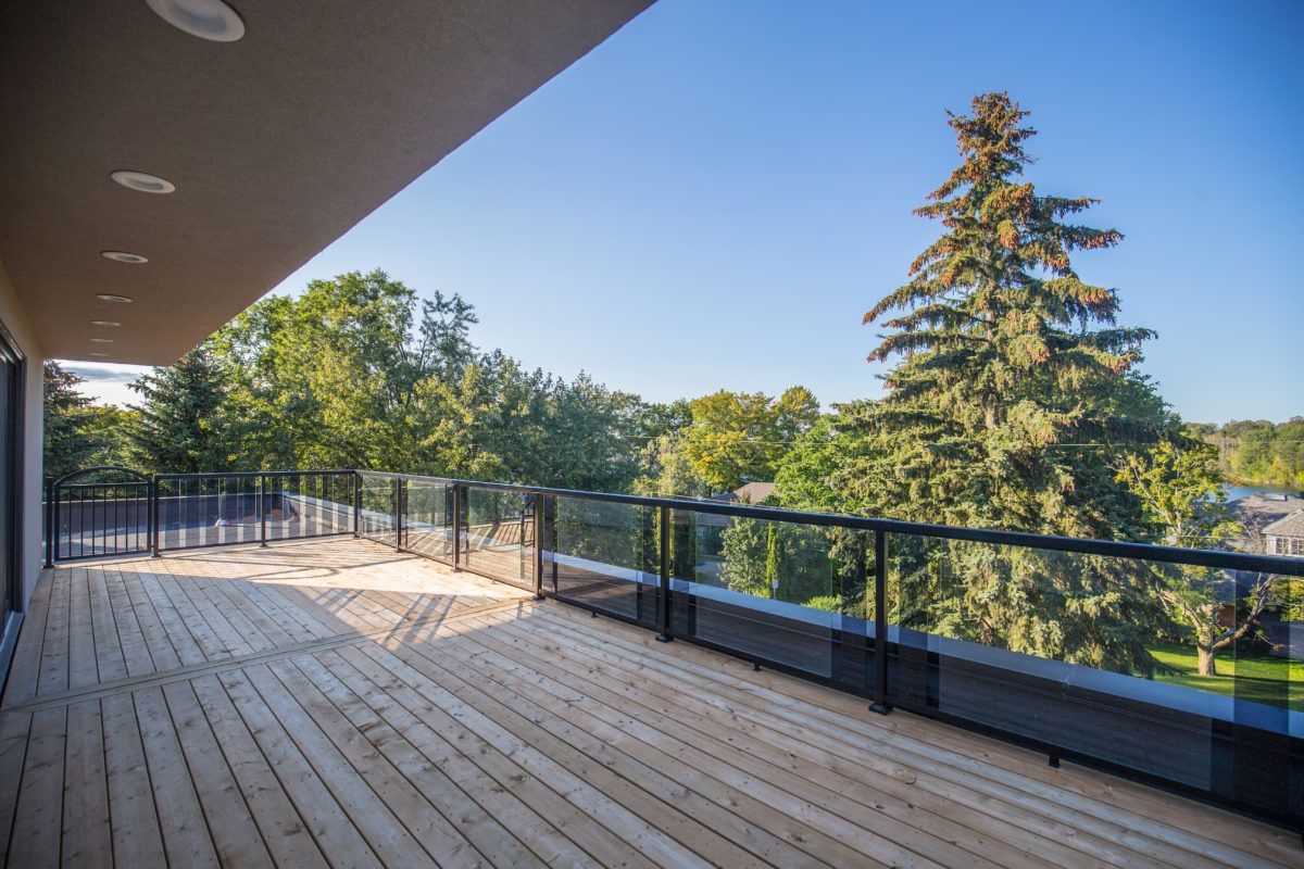 Spacious outdoor terrace of a 5000 sqft Toronto luxury home renovation featuring a wide wooden deck, modern glass railing system, and elevated balcony overlooking mature trees and scenic surroundings. This custom exterior living space enhances outdoor entertaining and relaxation with durable materials and clean contemporary design. Completed by Reno Compass Inc., a trusted Toronto renovation company specializing in high-end residential renovations and full-property transformations.