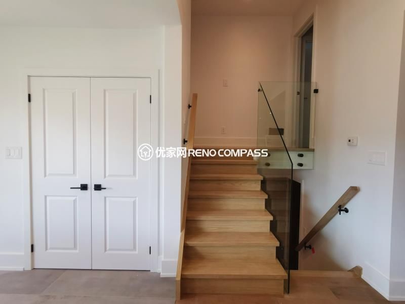 Modern staircase completed as part of a North York interior renovation, featuring solid wood treads, a frameless glass railing, and clean-lined handrails. The open glass guard enhances natural light flow while maintaining safety and visual openness. Adjacent custom double doors provide concealed storage, keeping the circulation area organized and uncluttered. This staircase renovation reflects a balanced approach to structure, function, and contemporary interior design by a Toronto renovation company.