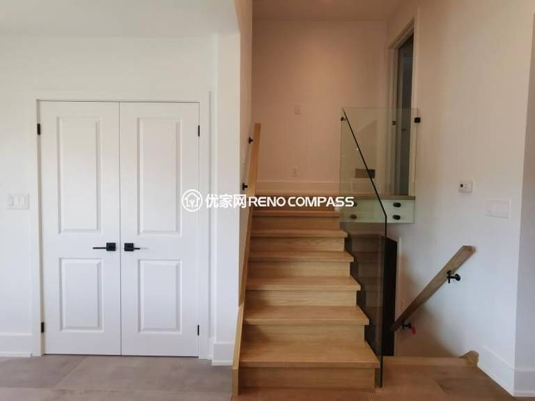 Modern staircase completed as part of a North York interior renovation, featuring solid wood treads, a frameless glass railing, and clean-lined handrails. The open glass guard enhances natural light flow while maintaining safety and visual openness. Adjacent custom double doors provide concealed storage, keeping the circulation area organized and uncluttered. This staircase renovation reflects a balanced approach to structure, function, and contemporary interior design by a Toronto renovation company.