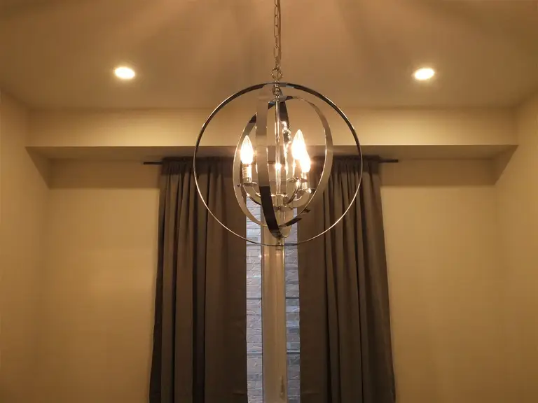 This Kleinburg interior renovation features a contemporary chandelier paired with recessed pot lights, creating a warm and elegant lighting design for the dining area. The modern circular chandelier adds a stylish focal point, while the ceiling pot lights provide balanced illumination throughout the space. Combined with large windows and neutral interior finishes, the lighting enhances the overall ambiance and sophistication of the renovated home.