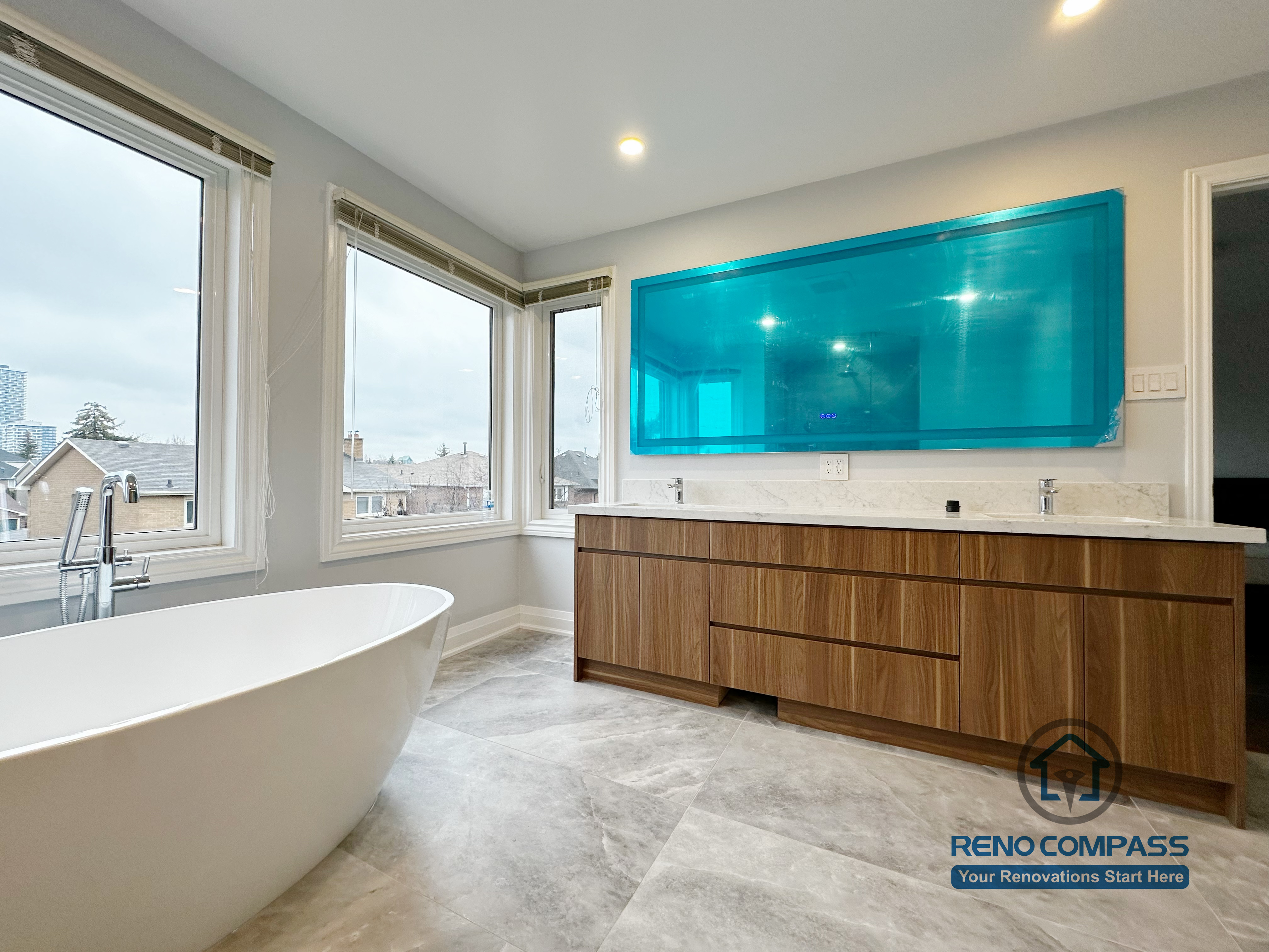 Bathroom renovation in Markham featuring a custom wood double vanity, quartz countertop, integrated mirrors, and a freestanding soaking tub. Large corner windows bring in natural light, creating a bright, spacious, and spa-inspired bathroom environment.