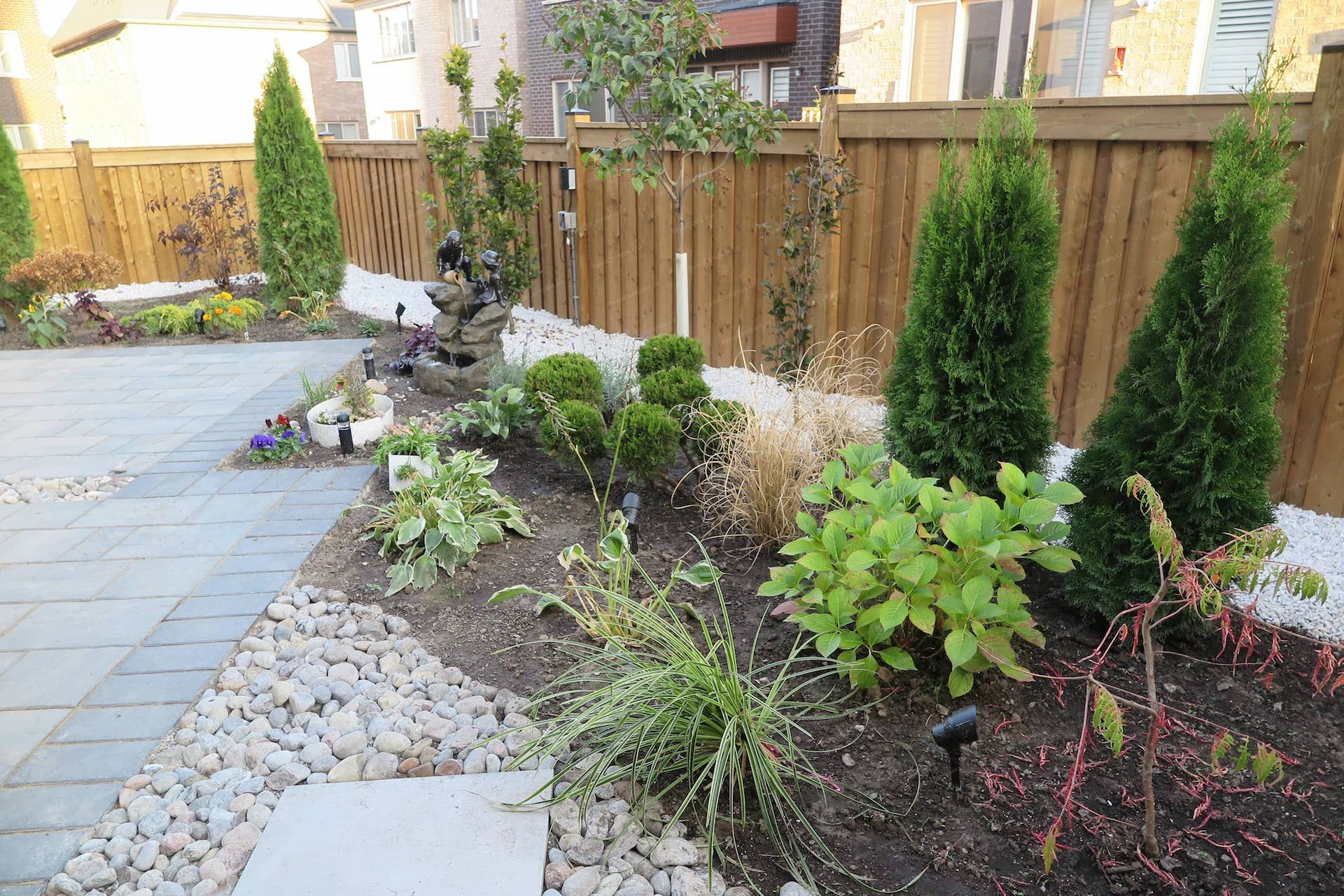 This Vaughan landscaping renovation showcases a clean interlock patio layout alongside a beautifully arranged garden bed with ornamental shrubs, flowering plants, and decorative river rock borders. The design adds color, structure, and a relaxing natural atmosphere to the backyard living space. Expertly completed by Reno Compass Inc