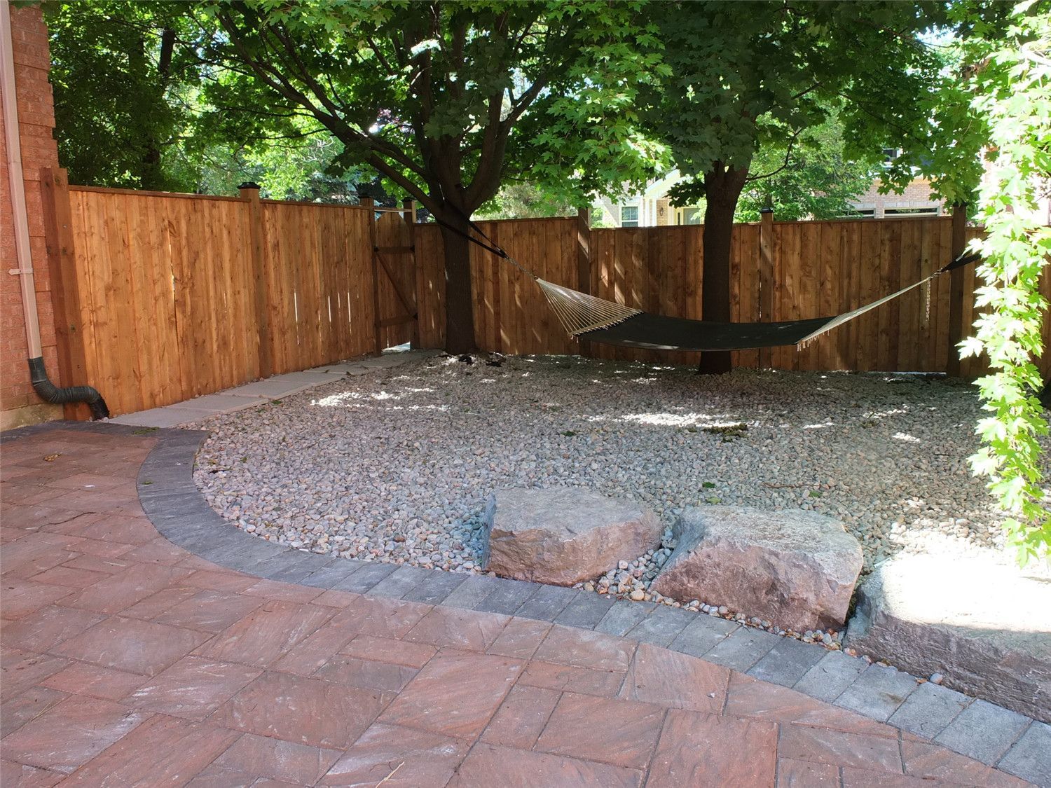 This Aurora landscaping renovation highlights a curved interlocking patio seamlessly integrated with a decorative gravel relaxation area. The contrasting stone border defines the transition between the paver surface and the natural stone feature zone, creating visual depth and balance.

Reno Compass Inc. carefully designed the layout to preserve mature trees while enhancing usability. The addition of river stone, large accent rocks, and a hammock-ready space transforms the backyard into a tranquil retreat that blends structure with nature.