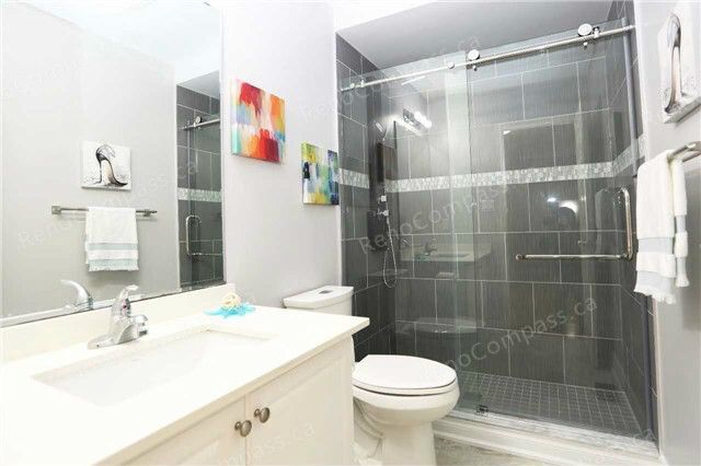 A modern bathroom remodel featuring a frameless glass shower, elegant grey tiles, and a crisp white vanity. This sleek Toronto renovation blends functionality with sophisticated design.